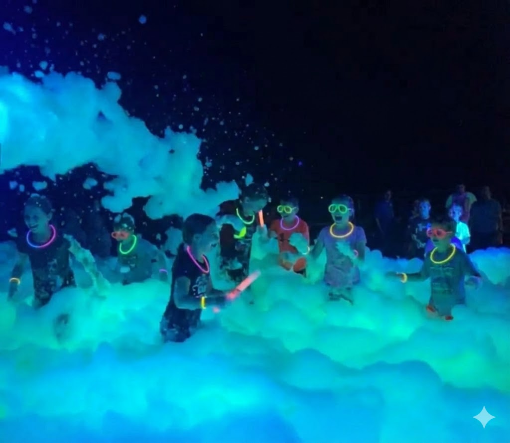 Kids playing in thick neon glowing foam at a glow foam party in Lexington NC, wearing glow necklaces and glasses under powerful UV blacklights.